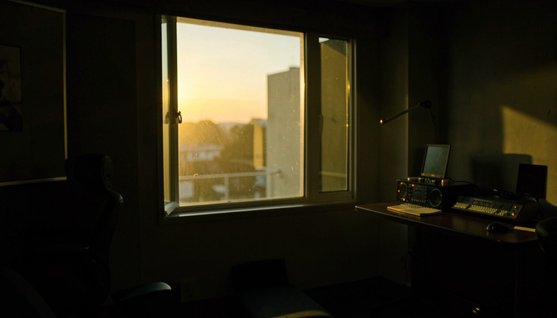 Warm golden light filtering through a broadcast studio window at dusk, with soft amber and olive tones blending into deep shadows